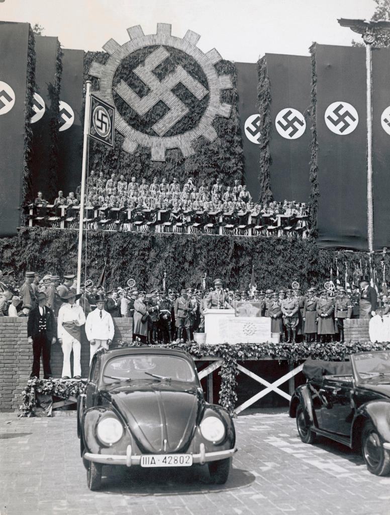 上图：1938年6月25日，希特勒在沃尔夫斯堡参加大众汽车厂的奠基仪式，前面是一辆大众甲壳虫汽车。希特勒上台后不久，就要求生产一种普通德国人买得起的「人民汽车」，可容纳2名成人和3名儿童、最高时速可达100km/h、最好采用风冷发动机，只卖990马克。奥地利工程师费迪南德·保时捷根据这一要求设计出著名的大众甲壳虫汽车。1936年10月12日，三辆大众VW-1下线。1938年，大众汽车公司在沃尔夫斯堡建厂，计划年产150万辆。二战期间，大众的生产能力被用于军备生产。德国人民所盼望的好处，最后都归于无有。正如圣经对大淫妇的预言：「你所看见的那十角与兽必恨这淫妇，使她冷落赤身，又要吃她的肉，用火将她烧尽」（启十七16）。兽其实并不喜欢大淫妇，只是暂时利用大淫妇迷惑世人。当大淫妇的价值被榨取干净之后，就会被付之一炬。